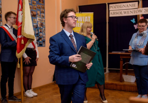 Tomek z nagrodą za bardzo dobre wyniki w nauce, na drugim planie poczet sztandarowy i wychowawczyni